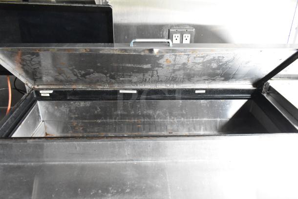 Open stainless steel food trailer storage compartment with labels "Truffle Max," "Sliced Tomato," and "Jared," showing rugged condition.