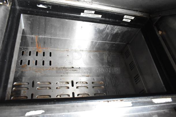 Interior of a stainless steel food trailer compartment with labeled sections for ingredients like lemon and roasted tomatoes.