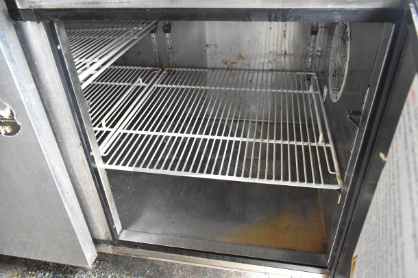Interior of a food trailer's stainless steel commercial fridge with wire shelving, showing signs of use.