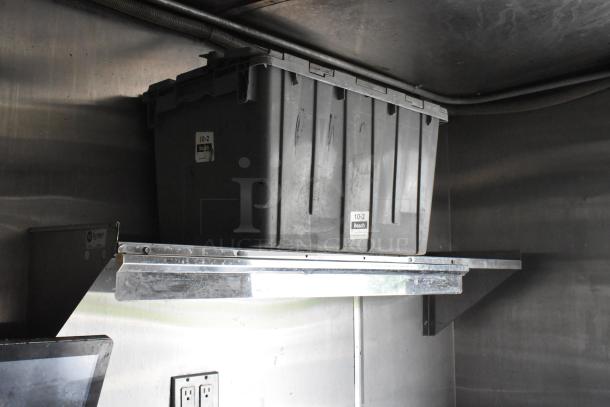 Gray storage bin labeled "10-2 Beach" on a metal shelf inside a food trailer. Industrial finish.