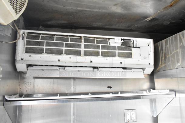 Interior view of a food trailer, showing a mounted ventilation or air conditioning unit against stainless steel walls, with signs of wear and age.