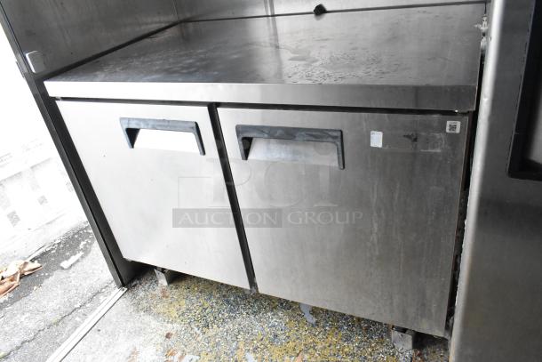 Stainless steel double-door commercial fridge in food trailer, durable, ready for use, minor surface wear.