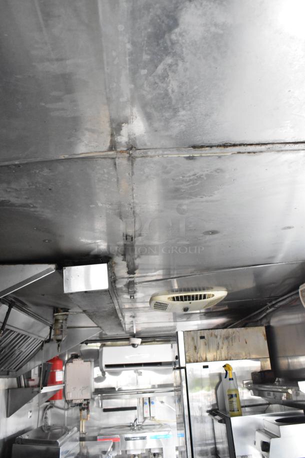 Interior view of a food trailer featuring stainless steel appliances, ventilation system, and various kitchen fixtures.