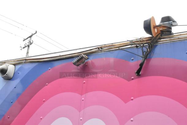 Colorful exterior of a food trailer with security camera, light, and cables on top, showcasing vibrant pink and blue design.