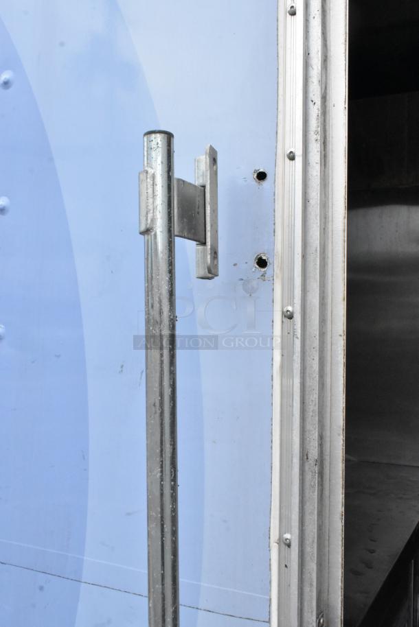 Close-up of a metal hinge and door edge on a fully outfitted food trailer, indicating wear and sturdy construction.