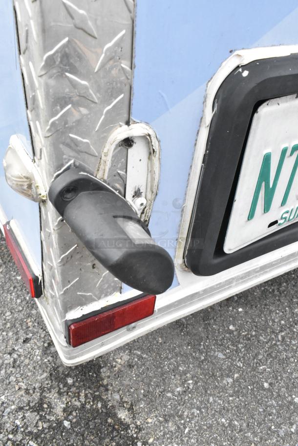Close-up of a food trailer’s corner with metal trim, red brake light, and partial license plate visible.