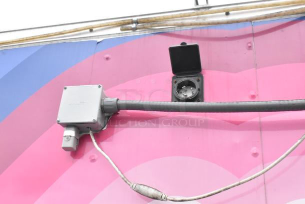 Electrical connection on a food trailer, featuring conduit and a CAMTEX junction box, on a colorful exterior.