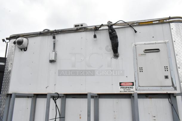 Food trailer exterior with security camera, electrical conduits, Noritz appliance, and propane warning label.