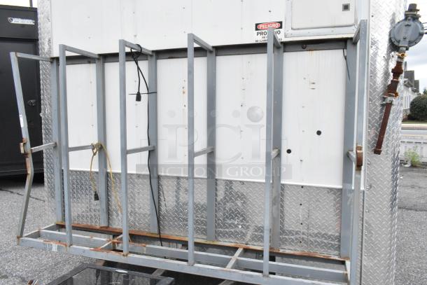 Food trailer exterior with metal framing, diamond plating, electrical cords, and a warning label.