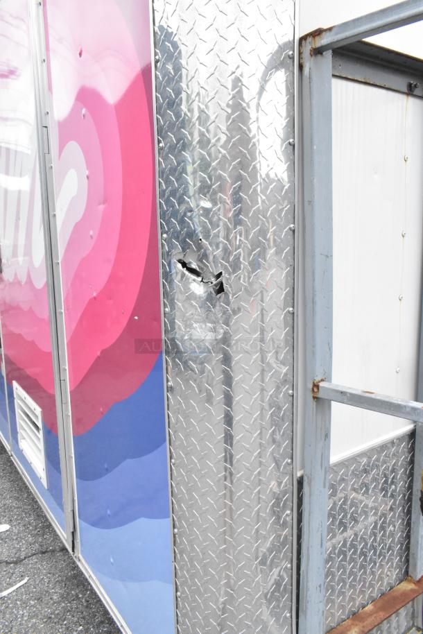 Food trailer exterior with colorful pink and blue decal. Features a dent and scratch on the metal siding. Ready for use.