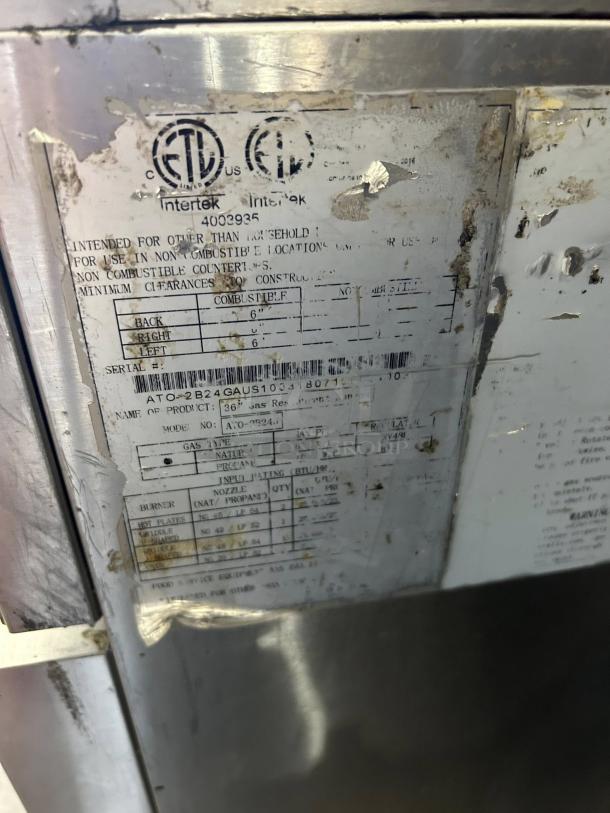 Worn label on Atosa AGR-2B24GR gas range stating compliance, model, and serial details with visible certification marks.
