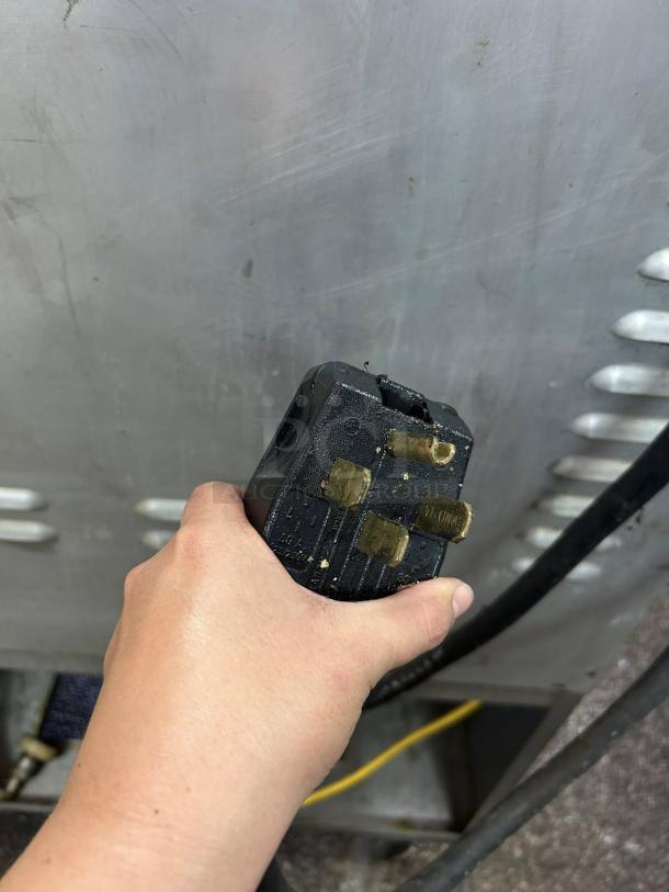 Hand holding black electrical plug for AutoFry MTI-40E ventless fryer, showcasing plug detail against metal backdrop.