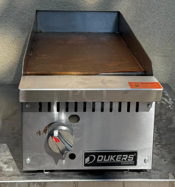 Dukers DCGM12 gas steel countertop griddle, visible dial, warning label. Used condition, durable construction.