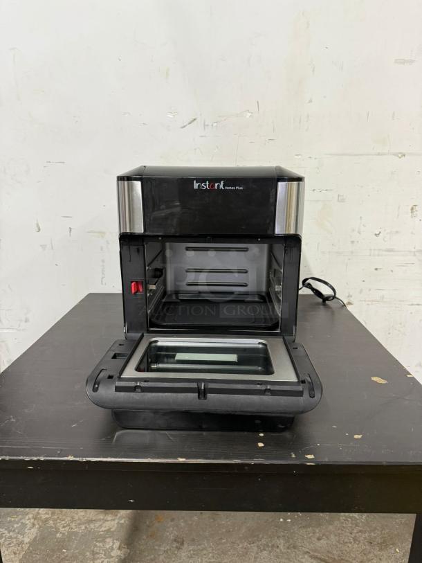 Instant Pot Vortex Plus 10, 7-in-1 air fryer toaster oven combo in black/stainless steel, model shown open on a table.
