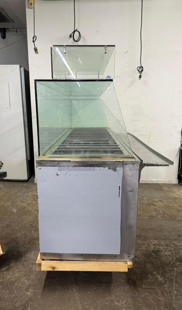 Stainless steel 12-pan steam table with glass sneeze guard. Some wear visible on surface. Ideal for food service.