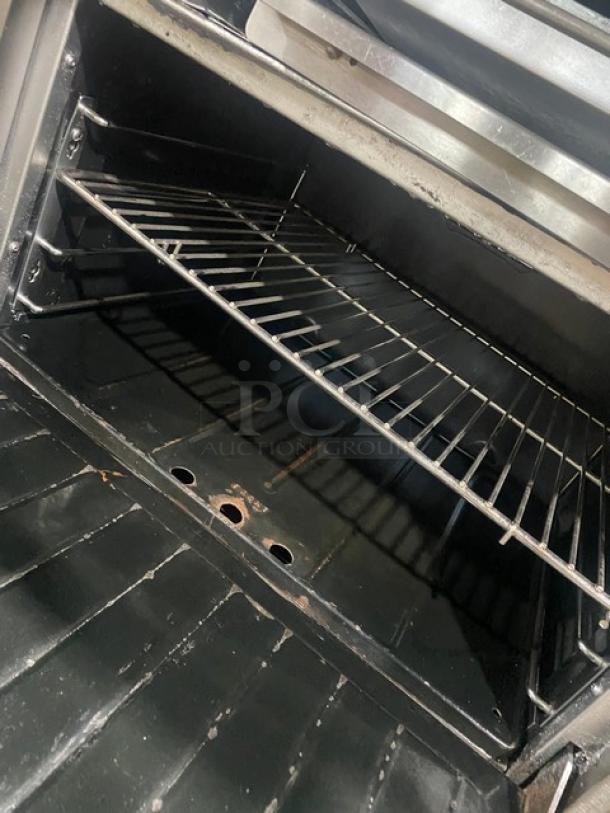 Garland stainless steel range with 6 burners, griddle, double oven, broiler, salamander shelf, model H283. Wired racks visible.