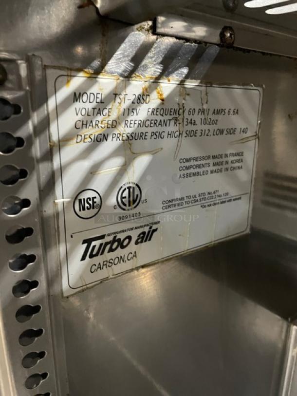 Turbo Air TST-28SD commercial stainless steel refrigerated prep table with cutting board. Model and specs label visible.