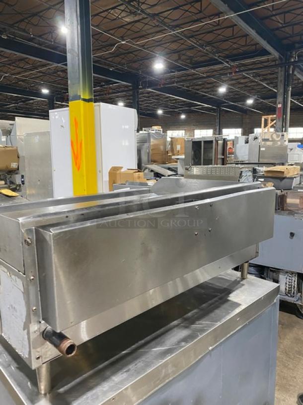 Globe stainless steel natural gas countertop griddle with back and side splash, on legs, commercial kitchen setting.