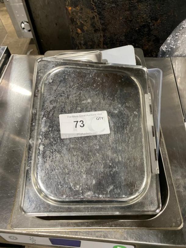 Lot of commercial stainless steel and polycarbonate pan lids, used condition, with auction tag "73" visible.