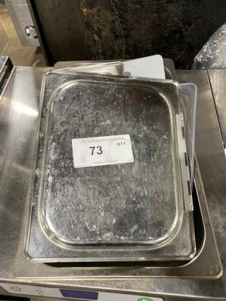 Lot of commercial stainless steel and polycarbonate pan lids, used condition, with auction tag "73" visible.