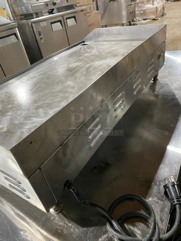 Cecilware stainless steel electric countertop flat griddle with thermostatic control, back and side splash, on legs. Plug visible.