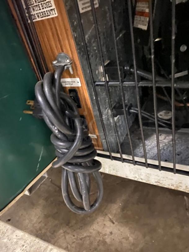 Coiled black power cord attached to the back of a commercial wooden style refrigerated meat deli display showcase.