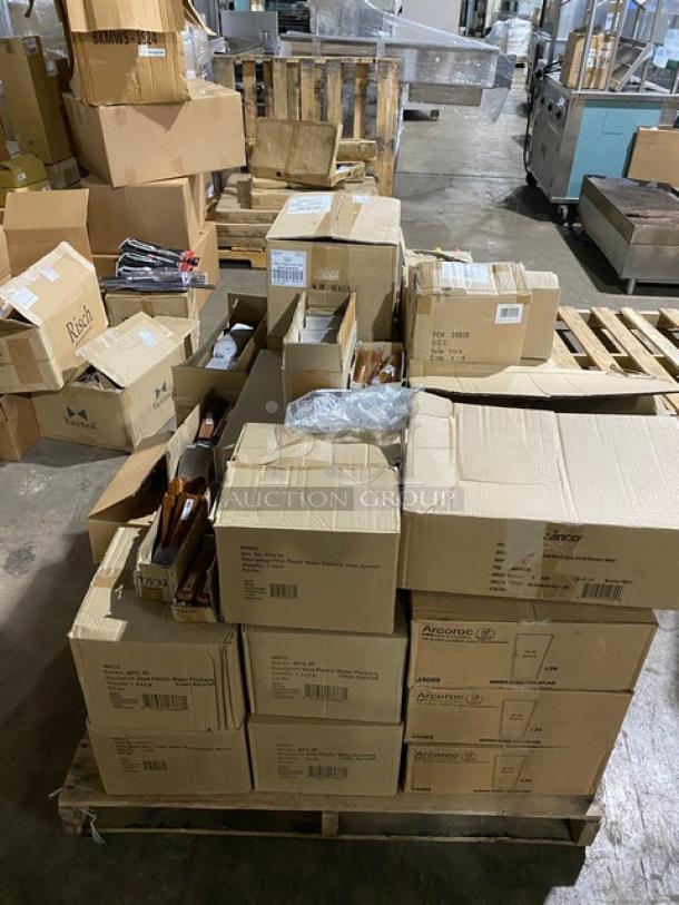Mixed pallet of new commercial kitchenware, including C.A.C. China porcelain dishes, Chef & Sommelier wine glasses, Walco teaspoons, Winco pitchers, Arcoroc glasses, and Winco turners. Boxes stacked on pallets.