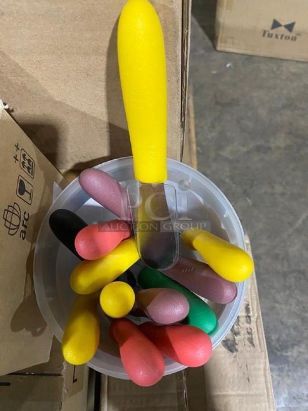 Container with colorful handle utensils, yellow, red, pink, green grips, on a cardboard box. Model: Tuxton.
