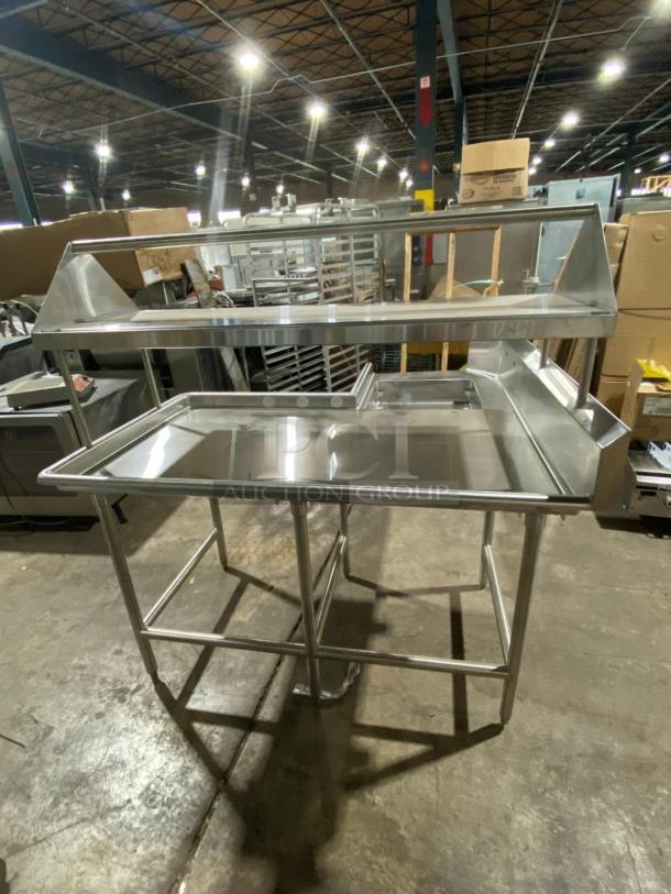 Brand new L-shaped stainless steel dishwashing station with single sink, double-sided slant rack, and shelving on legs.