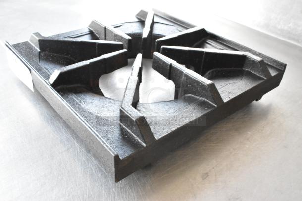 Brand new 12" x 12" cast iron spider grate, open top with built-in bowl, showing minor scratches and dents.