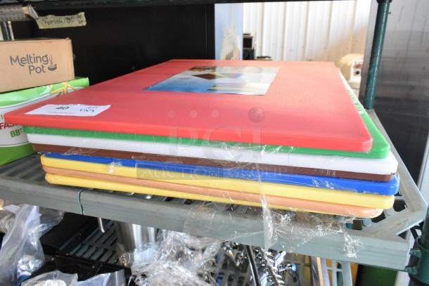 Nine new scratch and dent cutting boards, including Winco CBRD-1824, in various colors, wrapped in plastic, stacked on a shelf.