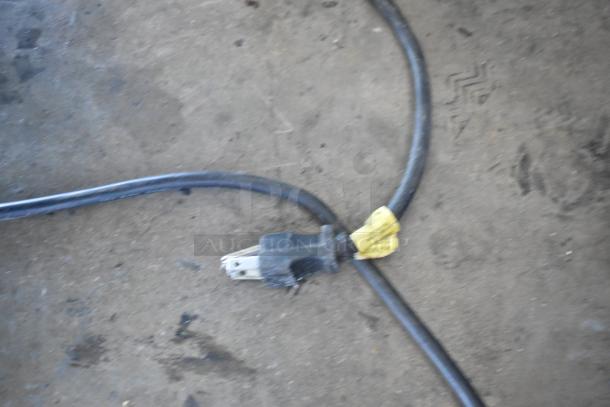 Cable with three-pronged plug on concrete floor, attached to yellow tag.