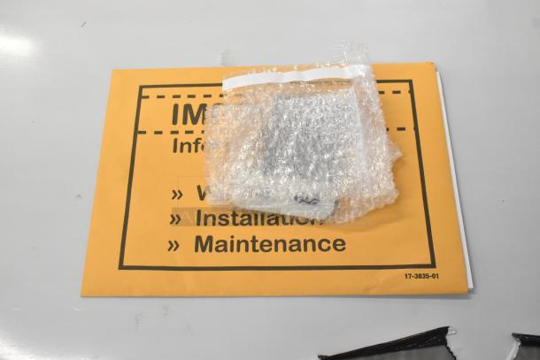 Yellow manual for Scotsman MC1030SA-32A ice machine, installation, and maintenance guide. Bubble-wrapped component on top.