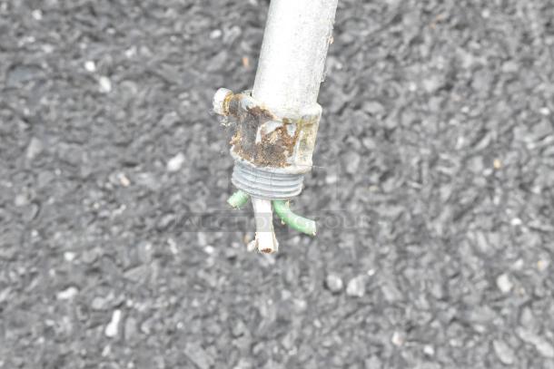 A close-up of a rusty metal pipe with exposed wires, showing wear and degradation against a textured asphalt background.