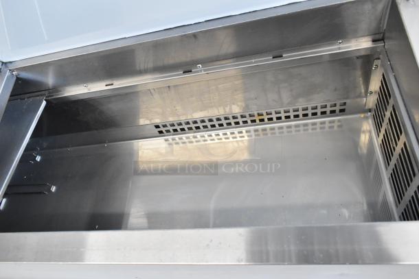 2024 Avantco 178SSPPT2 stainless steel pizza prep table interior, features oversized cutting board, shelves, and casters.