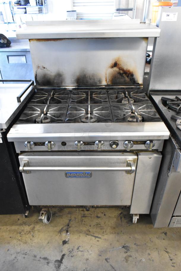 Imperial stainless steel commercial gas-powered 6-burner range with oven, overhead shelf, backsplash, and commercial casters.