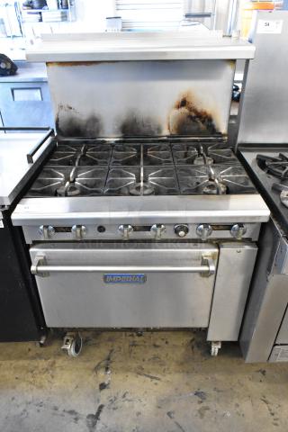 Imperial stainless steel commercial gas-powered 6-burner range with oven, overhead shelf, backsplash, and commercial casters.