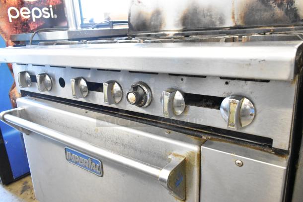 Imperial stainless steel commercial gas range with 6 burners, oven, overshelf, and backsplash on casters, shows wear.
