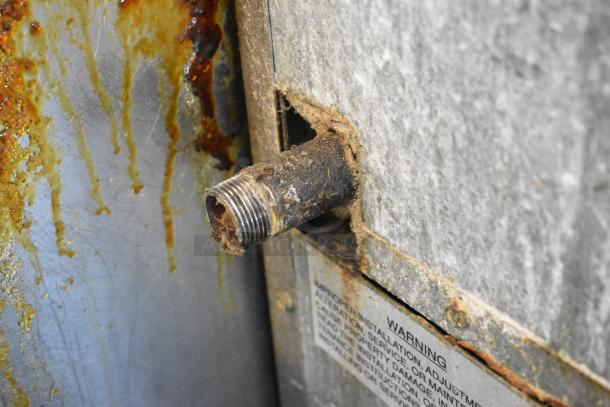 Close-up of a rusted pipe attachment on an Imperial stainless steel commercial gas range. Visible wear and corrosion.