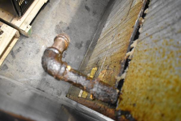 A close-up of a rusted and corroded pipe on the side of a heavy-duty appliance, possibly indicating wear and age.
