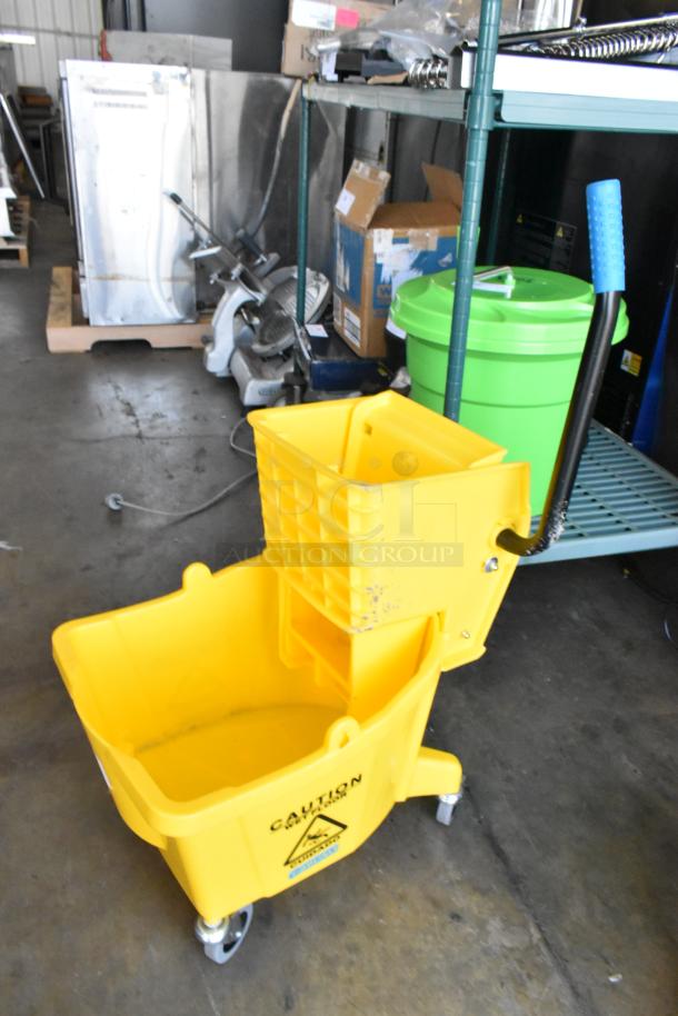 Yellow poly mop bucket with wringing attachment, on casters. Features caution sign on side. Good condition.