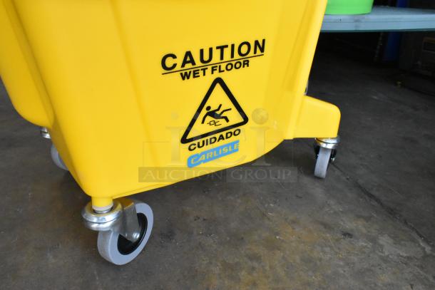 Yellow mop bucket with wringing attachment on casters, Carlisle brand. "Caution Wet Floor" label. Good condition.