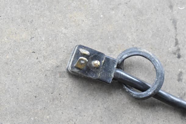 Close-up of a black power cord plug with visible prongs and loop on a concrete surface. Dirt present on the plug.
