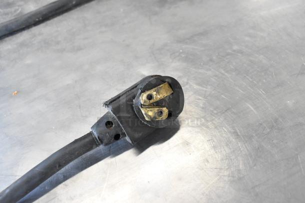 A close-up of a black three-prong electrical plug for a True TPP-67 pizza prep table, on a metallic surface.