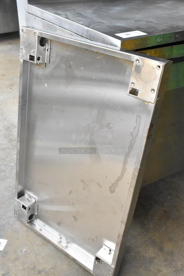Stainless steel panel with corner brackets, showing surface wear. Suitable for industrial or commercial use.