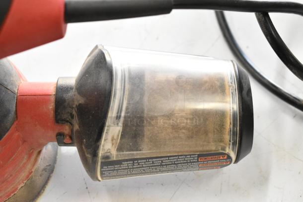 Red and black tool with clear dust collector, partially visible. Black cable attached. Dust inside the collector.