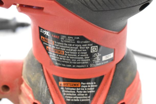 Skil 7492 grinder close-up, showing safety label and specifications: 120V, 60Hz, 2.8A, 5" (125mm), 12500 RPM.