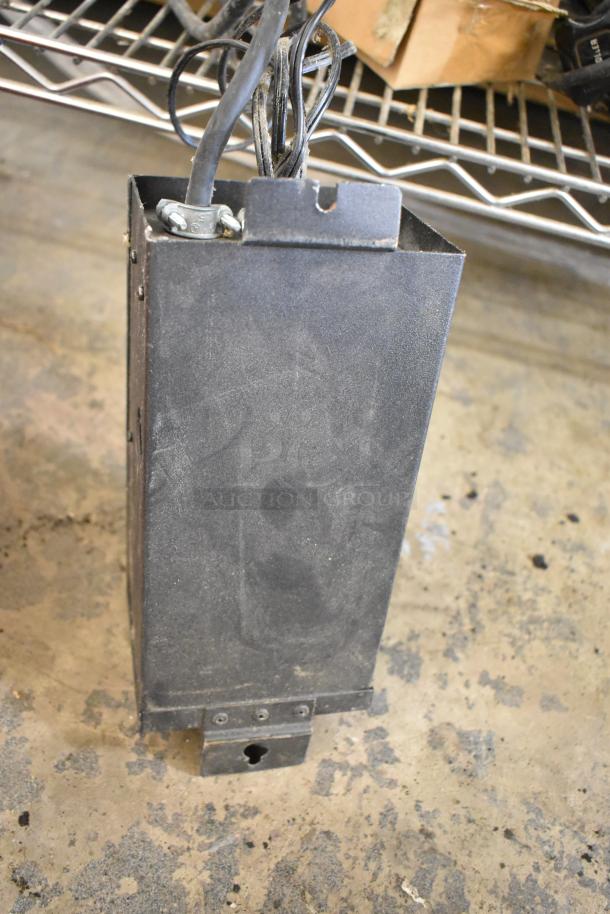 Metal box, likely housing transformer or electrical components, with visible wiring on top. Dusty surface, moderately worn condition.