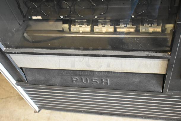 Metal commercial vending machine with key, features coin slots and "PUSH" labeled dispenser, in used condition.