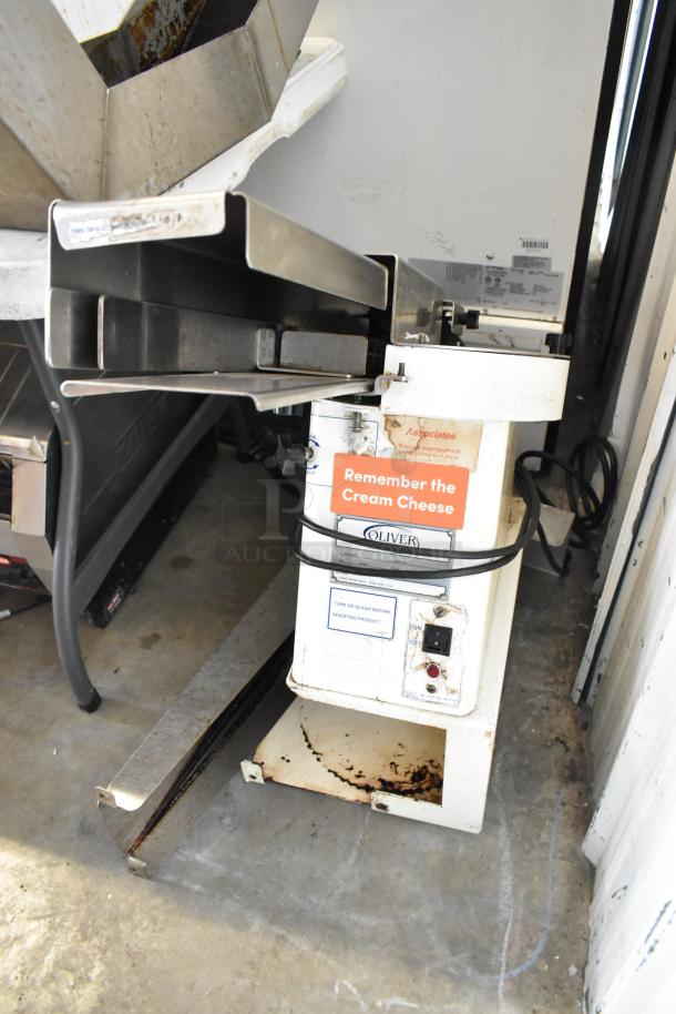 Oliver 702-N metal countertop bagel slicer, 115 volts, 1 phase. Displays wear and rust; operational labels visible.